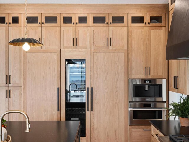 kitchen with stainless steel double oven, custom range hood, dark countertops, and light brown cabinets