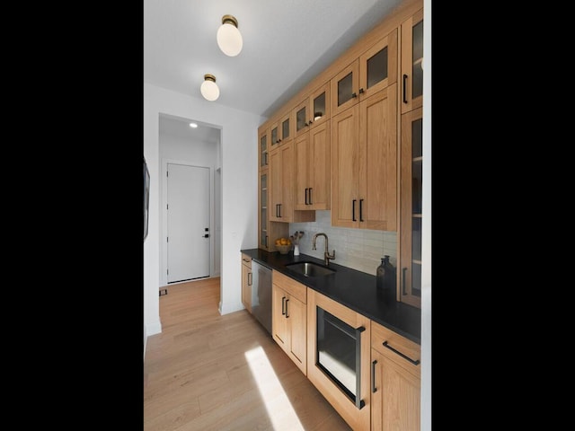 kitchen featuring tasteful backsplash, dark countertops, stainless steel dishwasher, light wood-style floors, and a sink