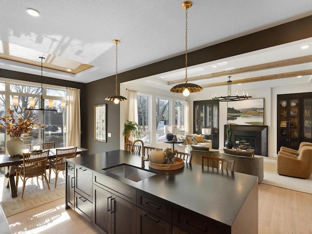 kitchen featuring dark countertops, open floor plan, a tray ceiling, pendant lighting, and a sink