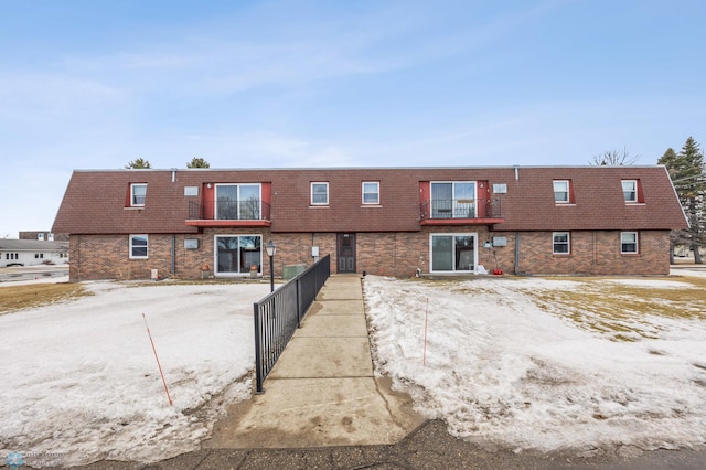 multi unit property featuring fence, mansard roof, and brick siding