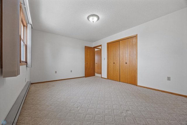 unfurnished bedroom featuring light carpet, baseboards, a textured ceiling, a baseboard heating unit, and a closet