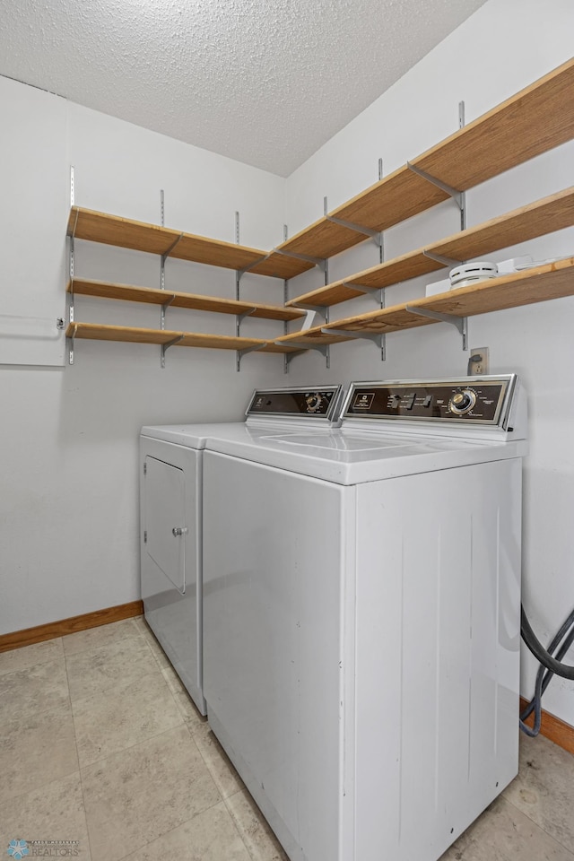 clothes washing area with a textured ceiling, laundry area, washing machine and dryer, and baseboards