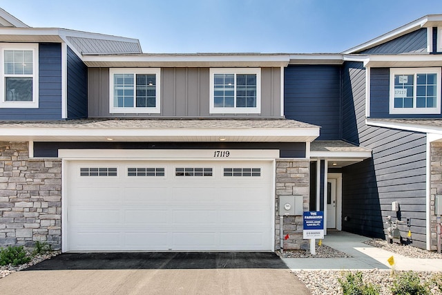 townhome / multi-family property featuring driveway, stone siding, a garage, and board and batten siding