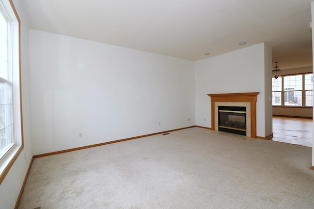 unfurnished living room featuring light carpet, a fireplace with flush hearth, baseboards, and a notable chandelier