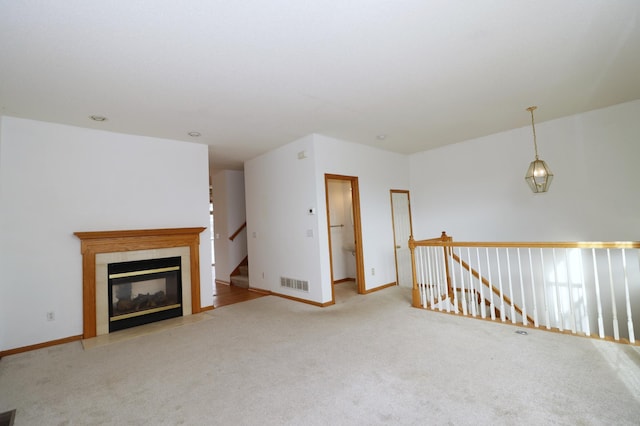 unfurnished living room with baseboards, a tile fireplace, visible vents, and light colored carpet