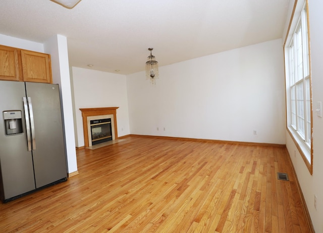 unfurnished living room featuring a fireplace with flush hearth, a wealth of natural light, visible vents, and light wood-style flooring