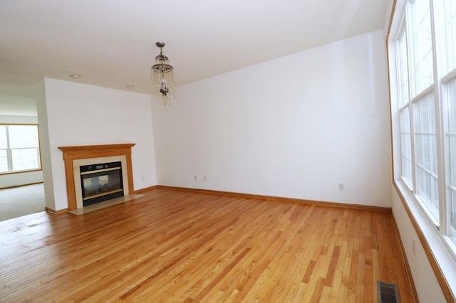 unfurnished living room with light wood finished floors, a fireplace with flush hearth, visible vents, and baseboards