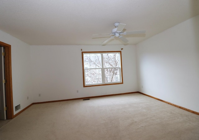 carpeted empty room with baseboards, visible vents, and a ceiling fan