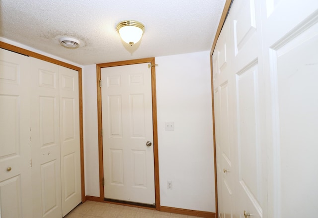 corridor with light floors, baseboards, visible vents, and a textured ceiling