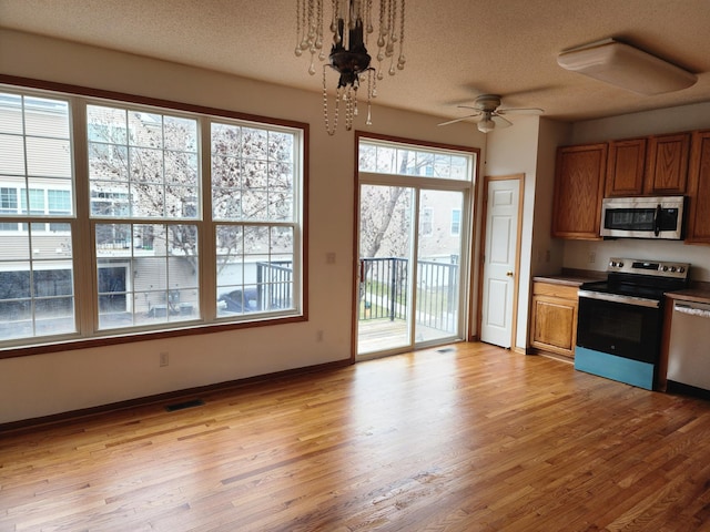 kitchen with brown cabinets, light wood-style flooring, pendant lighting, and stainless steel appliances