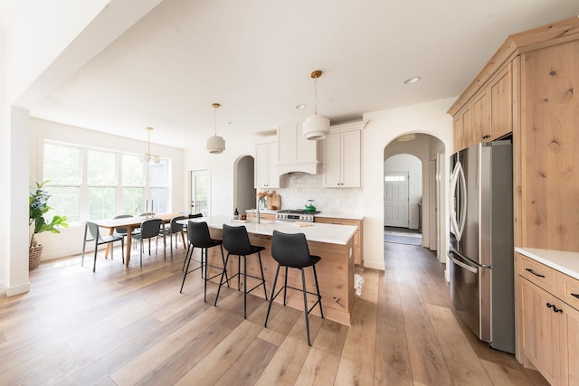 kitchen with arched walkways, custom exhaust hood, light countertops, backsplash, and freestanding refrigerator