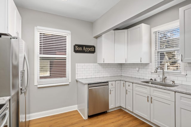 kitchen featuring light wood finished floors, stainless steel appliances, backsplash, white cabinets, and a sink