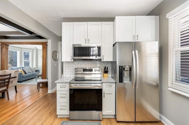 kitchen with appliances with stainless steel finishes, white cabinetry, backsplash, and light stone counters