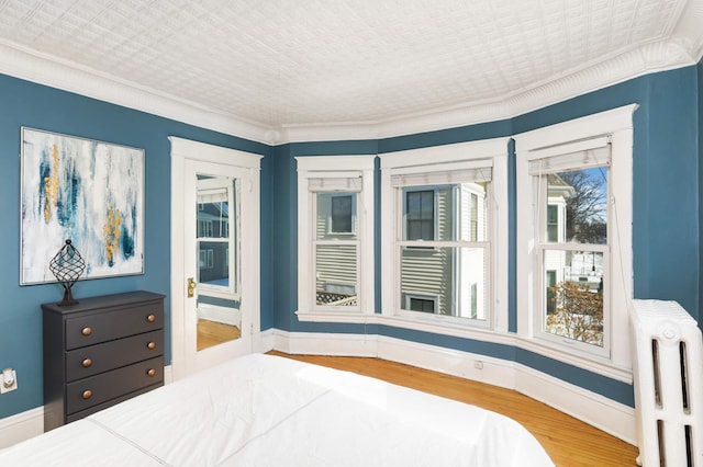 bedroom with crown molding, radiator heating unit, wood finished floors, and baseboards