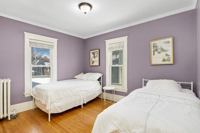 bedroom with light wood-style floors, radiator, ornamental molding, and baseboards