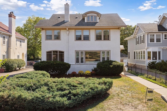 view of front of property featuring a shingled roof, brick siding, fence, a front lawn, and a chimney