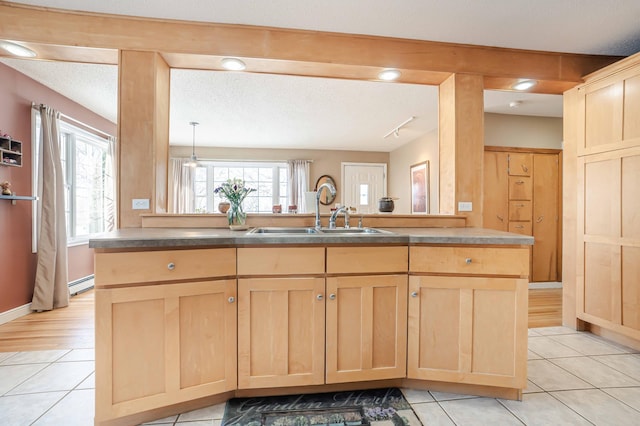 kitchen with light tile patterned floors, a baseboard radiator, a textured ceiling, light brown cabinetry, and a sink