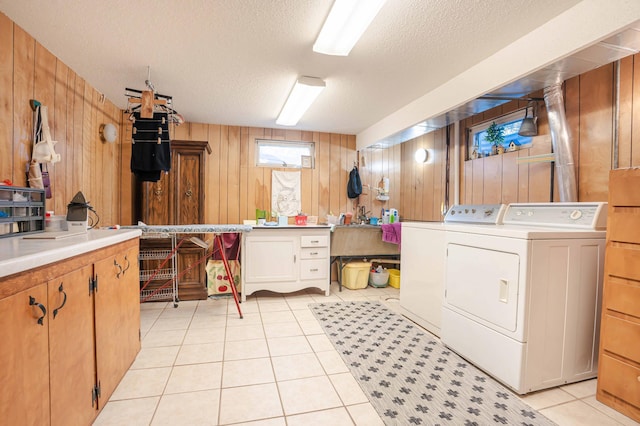 clothes washing area with washing machine and clothes dryer, cabinet space, light tile patterned flooring, wooden walls, and a textured ceiling