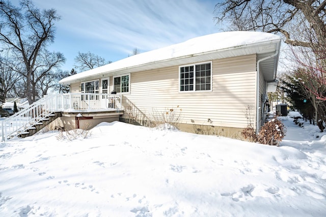 snow covered back of property featuring a garage, stairs, a wooden deck, and central AC unit