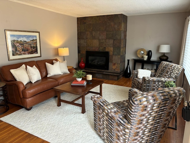 living room with a textured ceiling, wood finished floors, crown molding, and a tiled fireplace