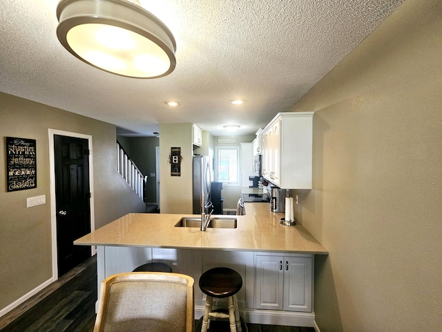 kitchen with a kitchen breakfast bar, freestanding refrigerator, a peninsula, light countertops, and white cabinetry