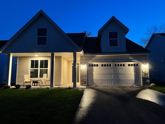 view of front of property featuring a front lawn, stone siding, covered porch, concrete driveway, and an attached garage