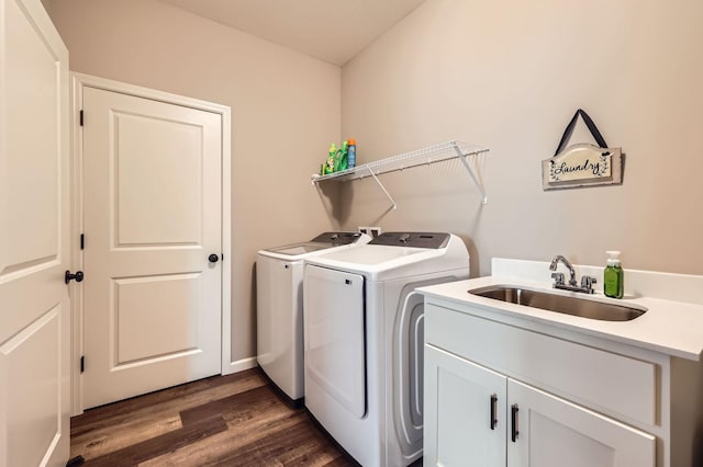 clothes washing area with dark wood finished floors, washing machine and clothes dryer, cabinet space, and a sink