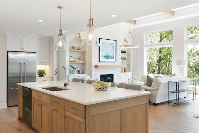 kitchen with a center island with sink, stainless steel built in refrigerator, light countertops, pendant lighting, and a sink