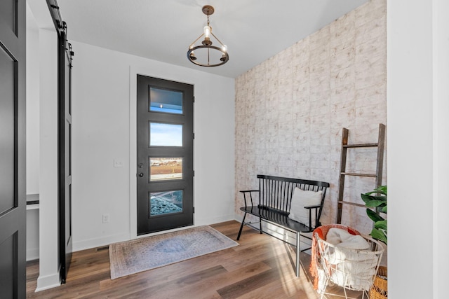 entrance foyer with a barn door, an inviting chandelier, dark wood finished floors, and baseboards