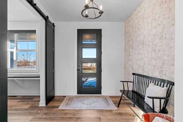 entrance foyer featuring wood finished floors, a notable chandelier, baseboards, and a barn door