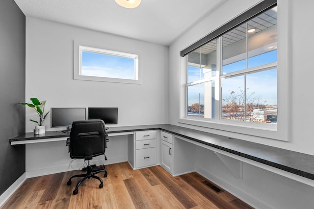 office space featuring baseboards, visible vents, built in desk, and light wood finished floors