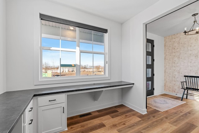 unfurnished office featuring dark wood-style floors, baseboards, visible vents, and a notable chandelier