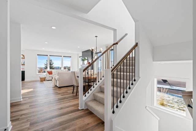 staircase with baseboards, wood finished floors, a fireplace, a chandelier, and recessed lighting