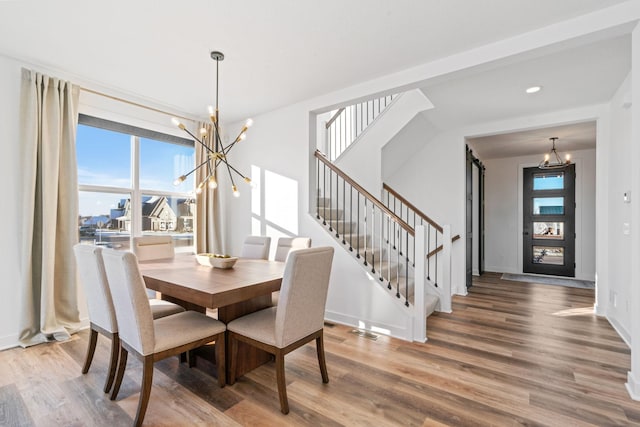 dining room with a barn door, visible vents, stairway, wood finished floors, and a chandelier