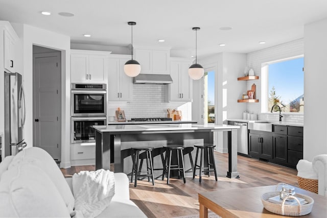 kitchen with light countertops, appliances with stainless steel finishes, a center island, wall chimney exhaust hood, and decorative light fixtures