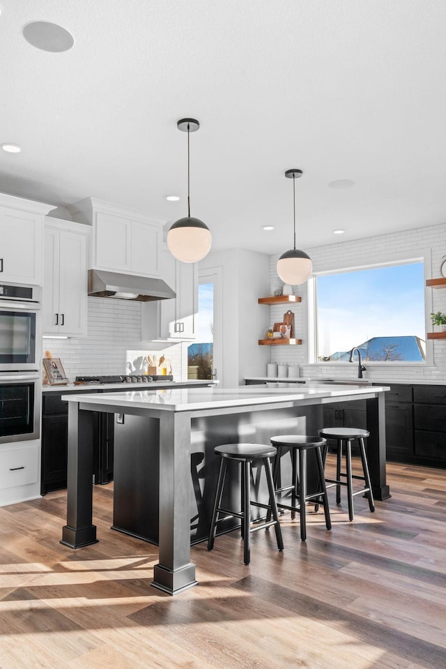 kitchen with a center island, light countertops, under cabinet range hood, white cabinetry, and open shelves