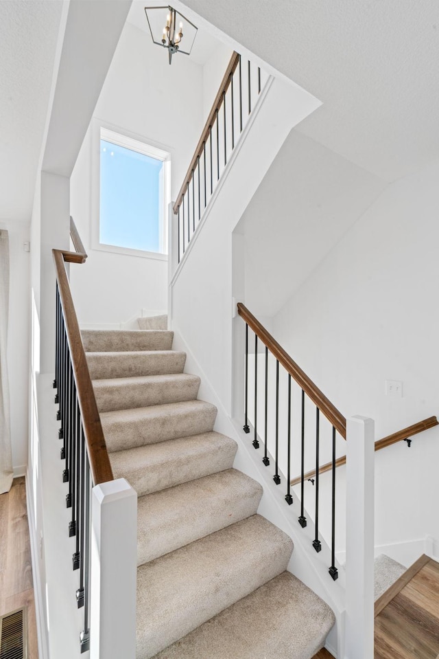 stairway featuring visible vents, a notable chandelier, baseboards, and wood finished floors