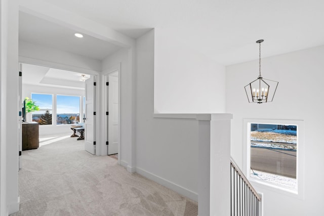 hallway with baseboards, recessed lighting, an inviting chandelier, and light colored carpet