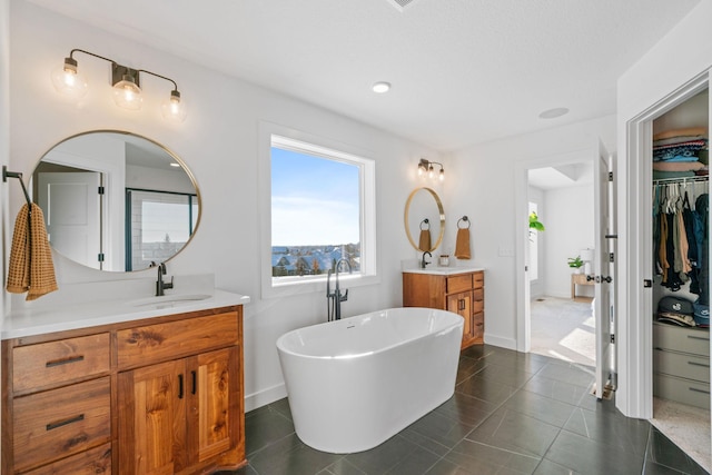 bathroom featuring tile patterned floors, a sink, a walk in closet, a freestanding bath, and two vanities