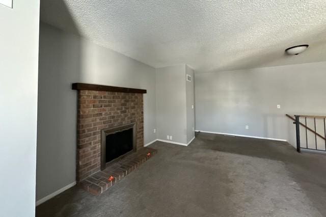 unfurnished living room featuring a textured ceiling, dark carpet, a fireplace, and baseboards