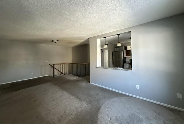 spare room featuring dark colored carpet, a textured ceiling, and baseboards