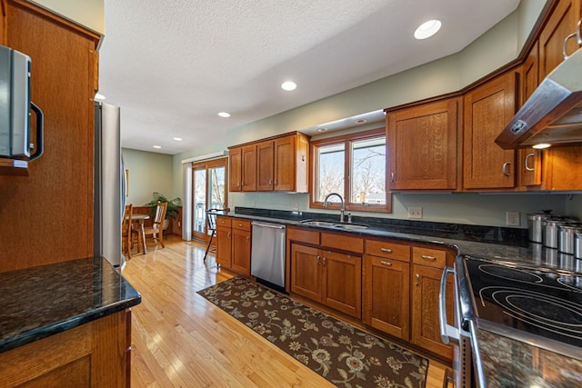 kitchen featuring brown cabinetry, appliances with stainless steel finishes, range hood, light wood-style floors, and a sink