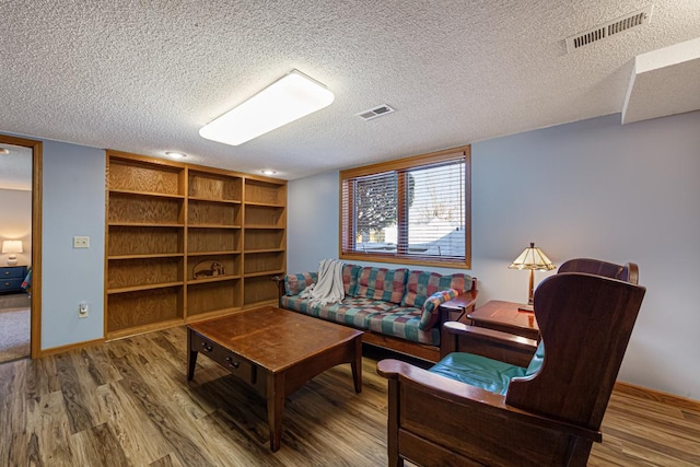 sitting room featuring visible vents, a textured ceiling, and wood finished floors