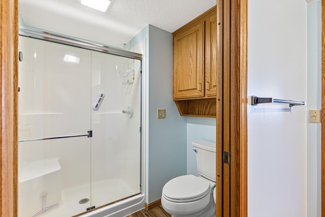 bathroom with a textured ceiling, a shower stall, and toilet