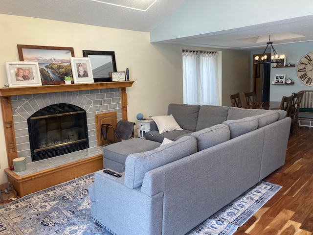 living room with dark wood-type flooring, lofted ceiling, a chandelier, and a fireplace