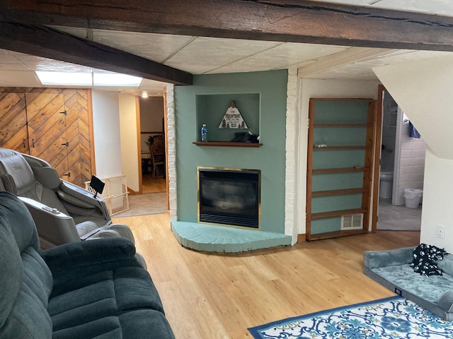 living room featuring beam ceiling, a fireplace, visible vents, wood walls, and wood finished floors