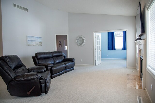 living room featuring a fireplace with flush hearth, visible vents, baseboards, and light colored carpet