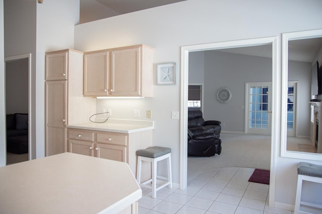 kitchen with light tile patterned floors, light colored carpet, open floor plan, light countertops, and light brown cabinetry