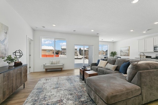 living room featuring light wood-type flooring, a textured ceiling, and recessed lighting