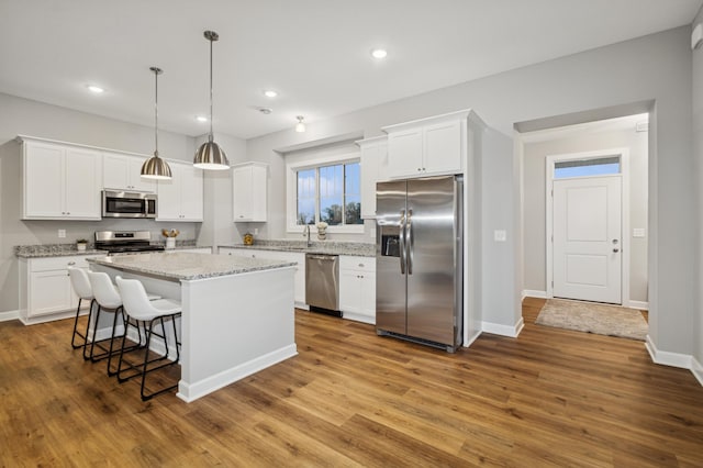 kitchen with stainless steel appliances, a center island, white cabinetry, and wood finished floors